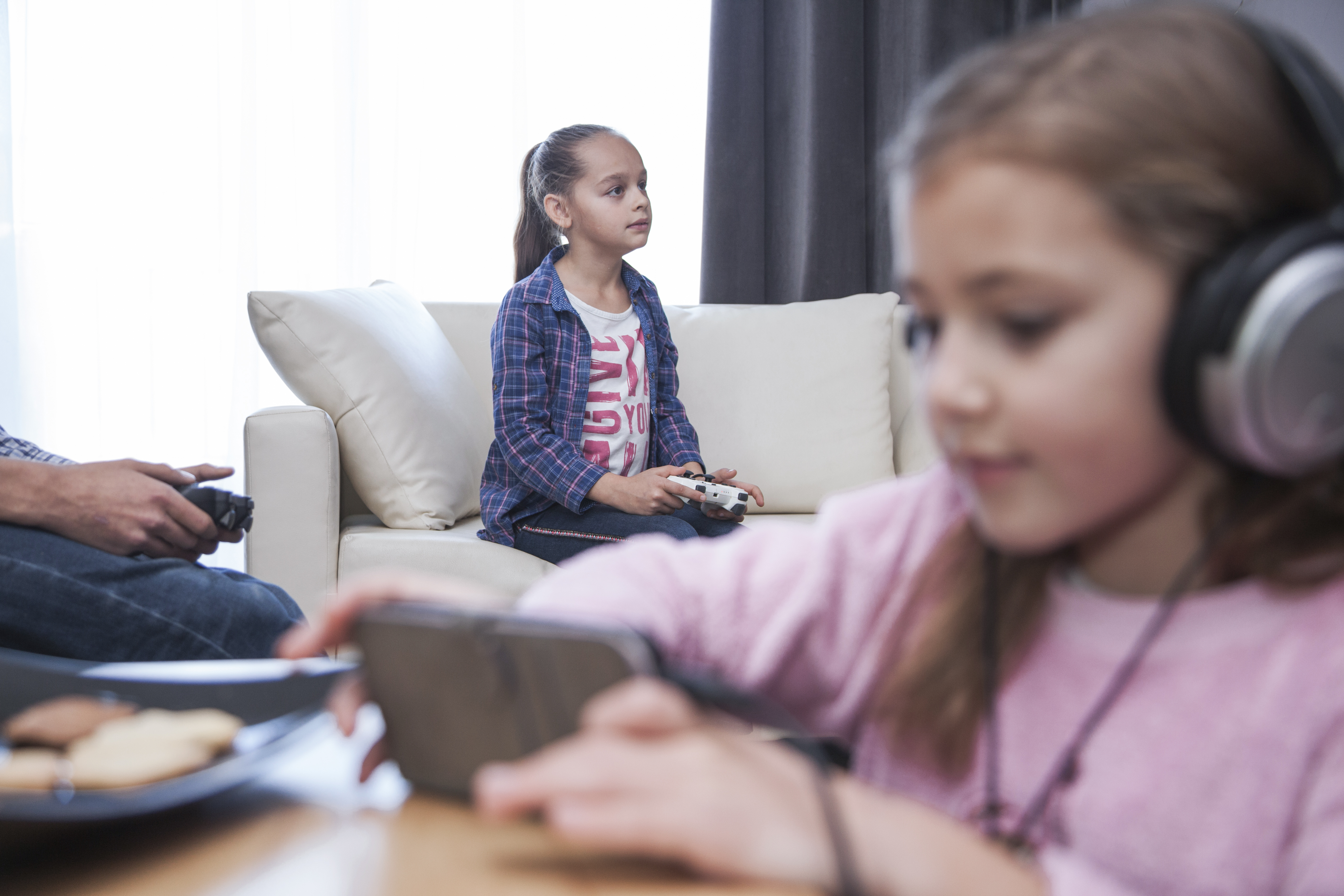 girl-with-smartphone-near-siblings-playing-video-gamens